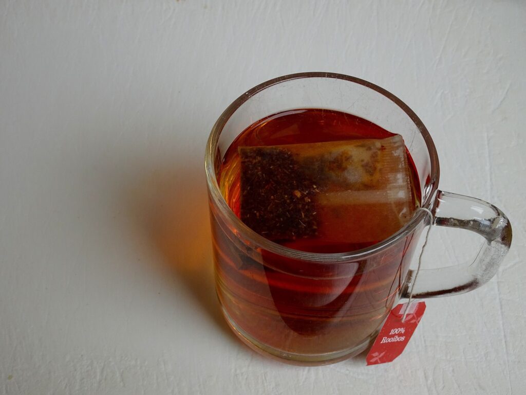 A glass mug of clear reddish-amber rooibos tea with the teabag in it.