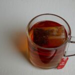 A glass mug of clear reddish-amber rooibos tea with the teabag in it.