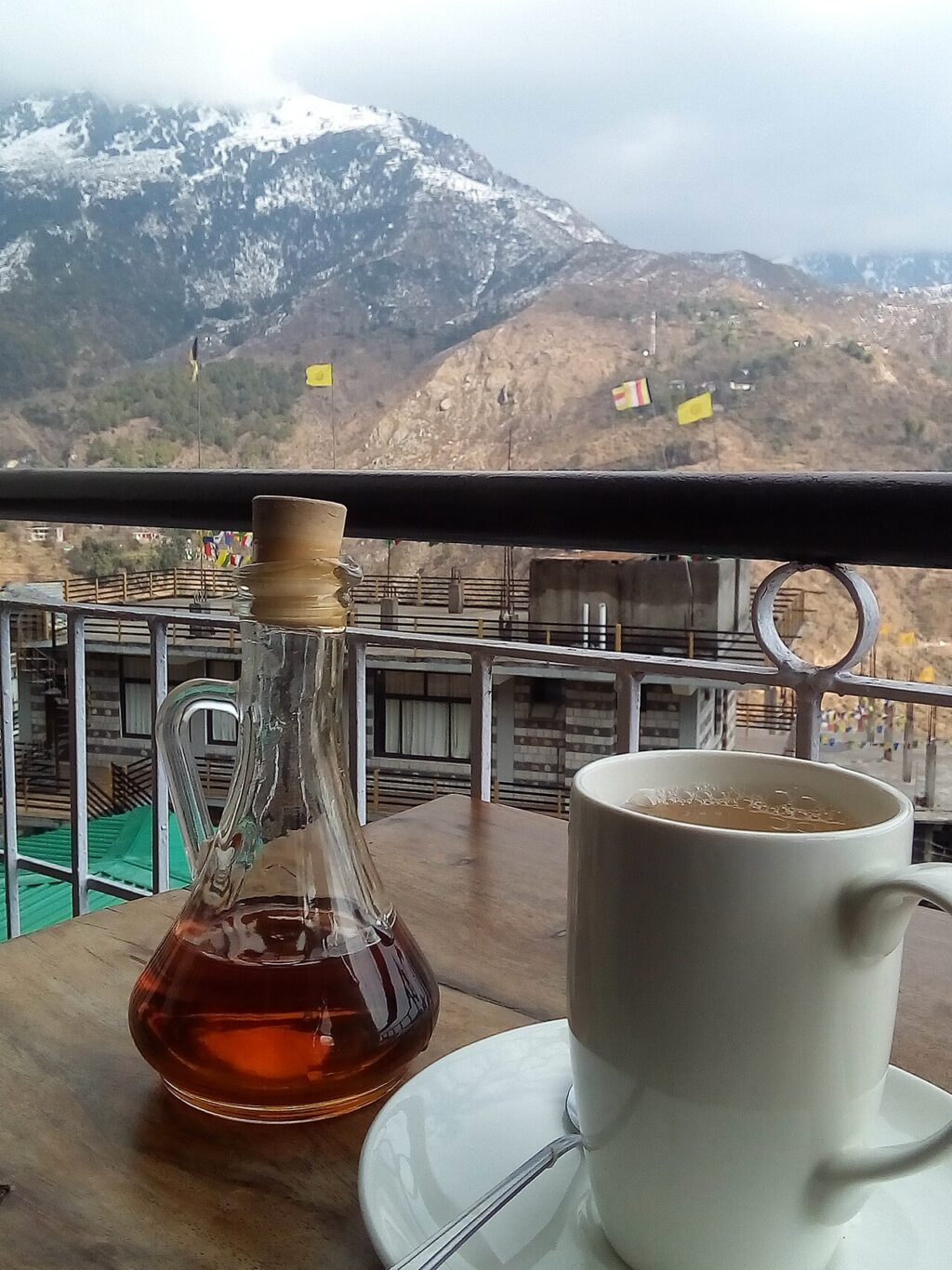A white mug of hot lemon and ginger tea on a saucer beside a glass bottle of honey, with mountains behind.