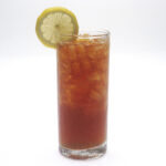 A tall glass of amber iced tea filled with ice, with a lemon slice on the rim, against a white background.