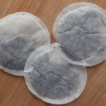 Three round, stringless tea bags filled with black tea lying on a wooden board.