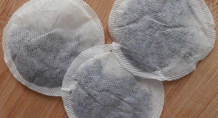 Three round, stringless tea bags filled with black tea lying on a wooden board.