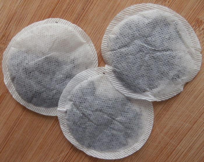 Three round, stringless tea bags filled with black tea lying on a wooden board.