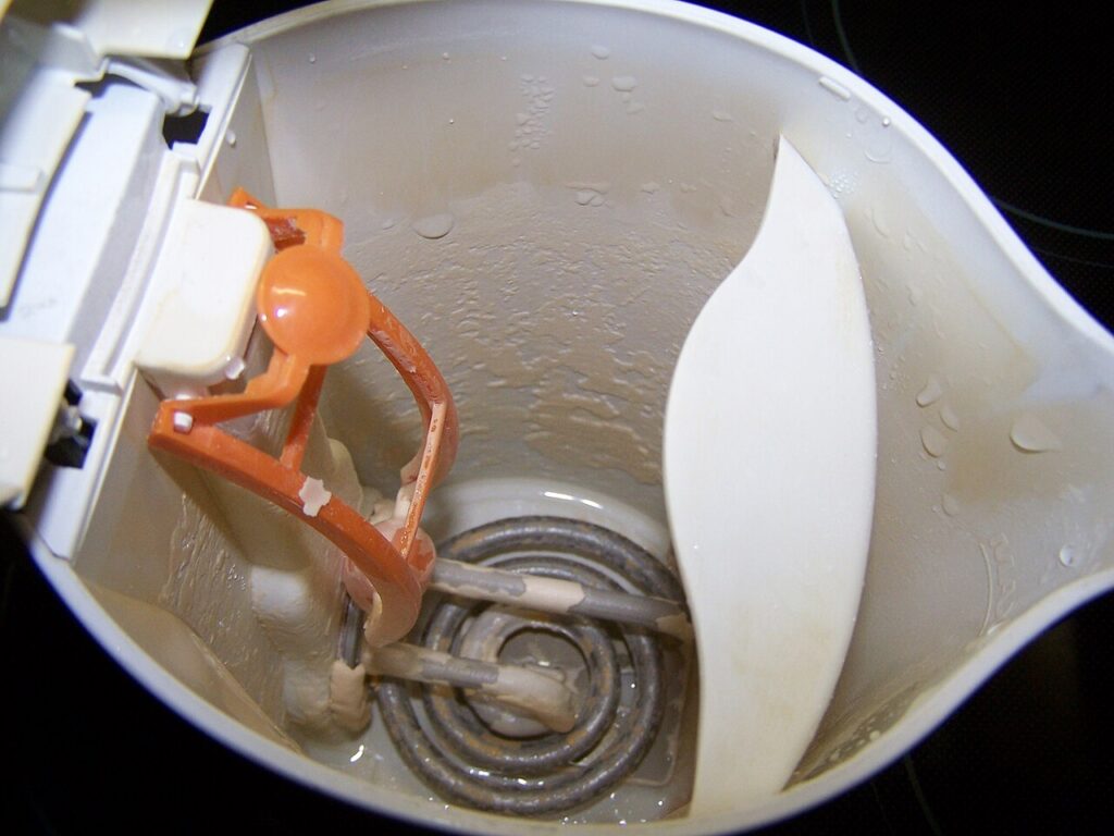 Inside of a white plastic electric kettle with a coiled heating element coated in pale limescale.