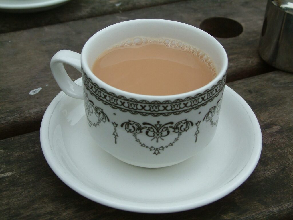 A white china cup and saucer with a black pattern, holding milky black tea, on a wooden table.