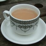 A white china cup and saucer with a black pattern, holding milky black tea, on a wooden table.