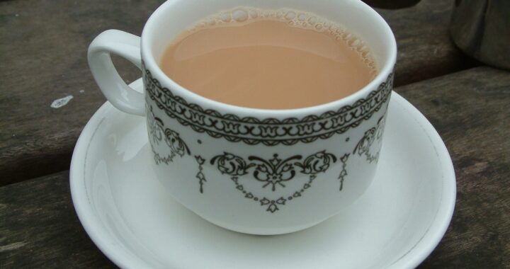 A white china cup and saucer with a black pattern, holding milky black tea, on a wooden table.