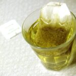 A small glass of pale golden chamomile tea with the teabag steeping in it, on a white cloth.