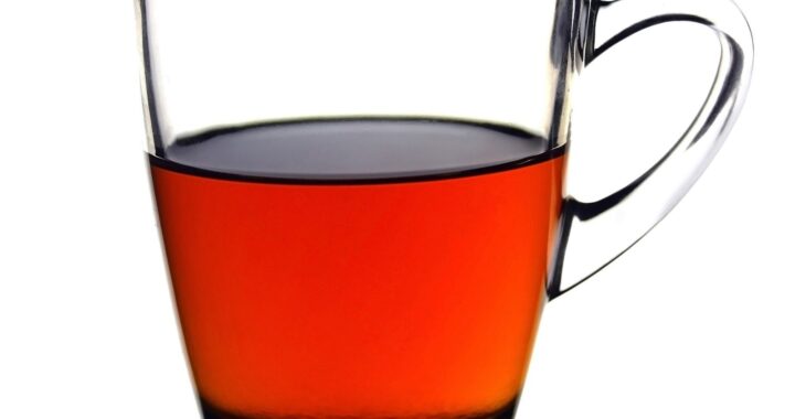 A clear glass mug half full of bright reddish-amber black tea against a white background.