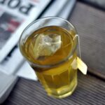 A glass of golden fennel tea with the teabag in it, standing on a newspaper.
