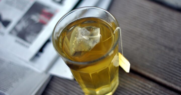 A glass of golden fennel tea with the teabag in it, standing on a newspaper.