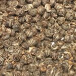 A close view of hundreds of small hand-rolled jasmine tea pearls, pale green and silver with flecks of dried petal.