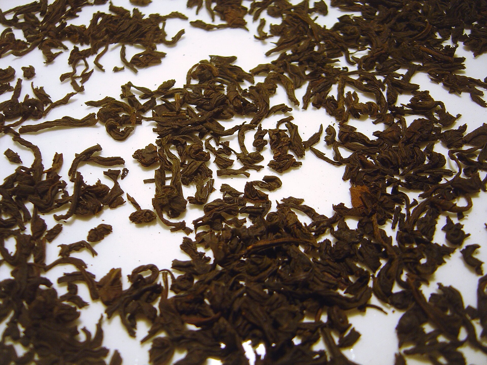 Twisted, very dark brown, almost black lapsang souchong tea leaves scattered on a white surface.