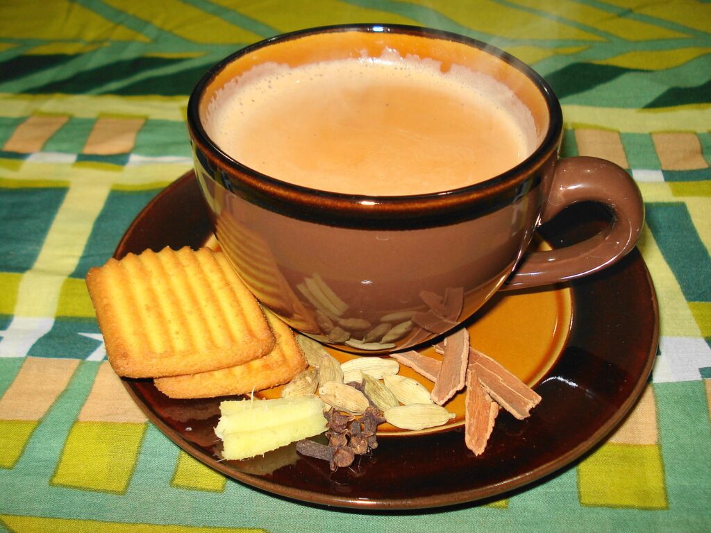 A brown cup of milky masala chai on a saucer with crackers, cinnamon, cardamom and ginger.