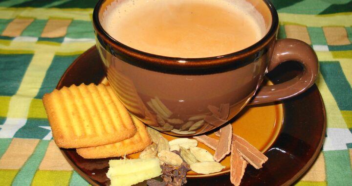 A brown cup of milky masala chai on a saucer with crackers, cinnamon, cardamom and ginger.