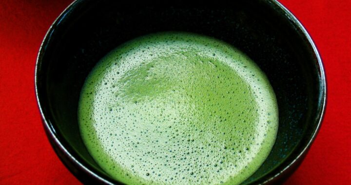 A black bowl of bright green, frothy whisked matcha on a red tray.