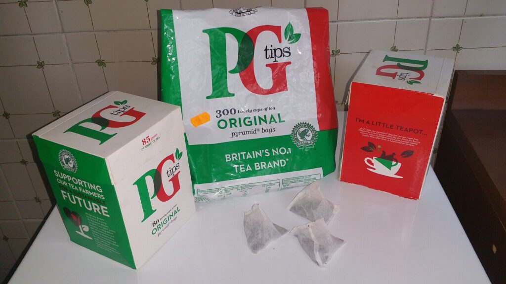 Three boxes of PG Tips tea with pyramid tea bags in front, on a kitchen counter.