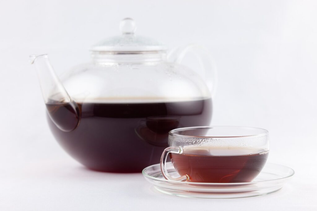 A glass teapot and a glass cup of dark reddish-brown pu-erh tea against a white background.