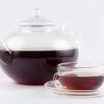 A glass teapot and a glass cup of dark reddish-brown pu-erh tea against a white background.