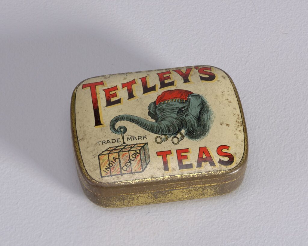 An old tin printed with Tetley's Teas in red and black and an elephant carrying tea chests.