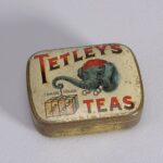 An old tin printed with Tetley's Teas in red and black and an elephant carrying tea chests.