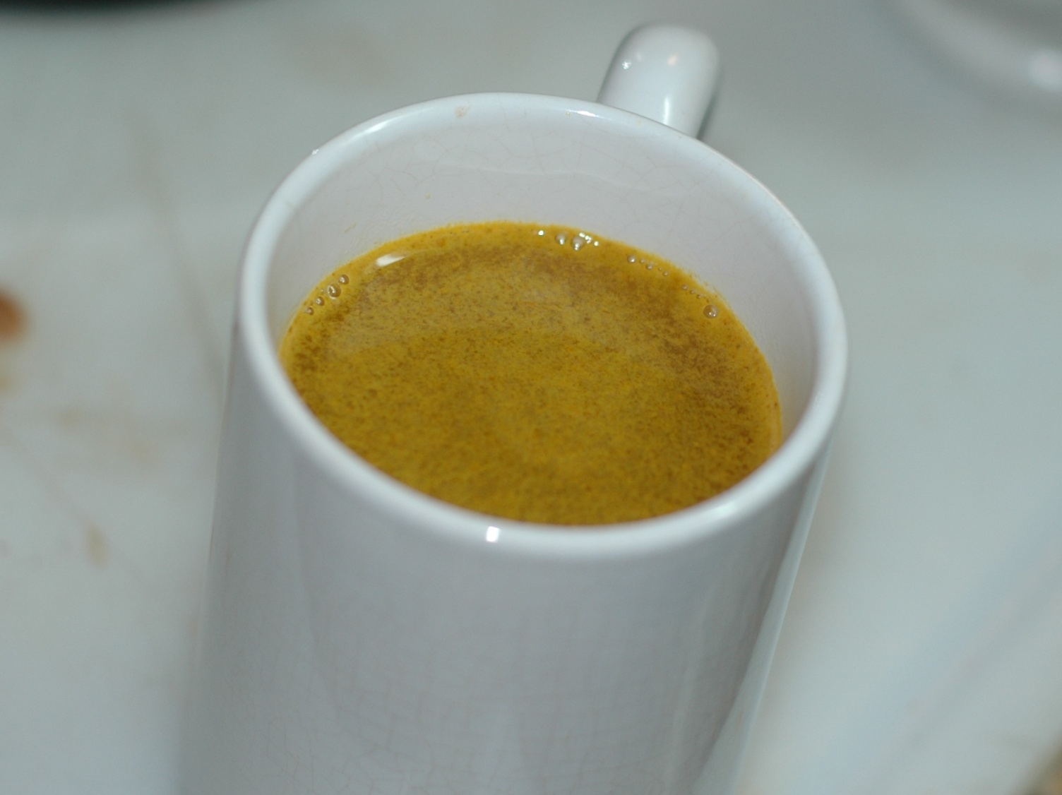 A white mug filled with cloudy golden-orange turmeric tea, seen from above on a pale table.