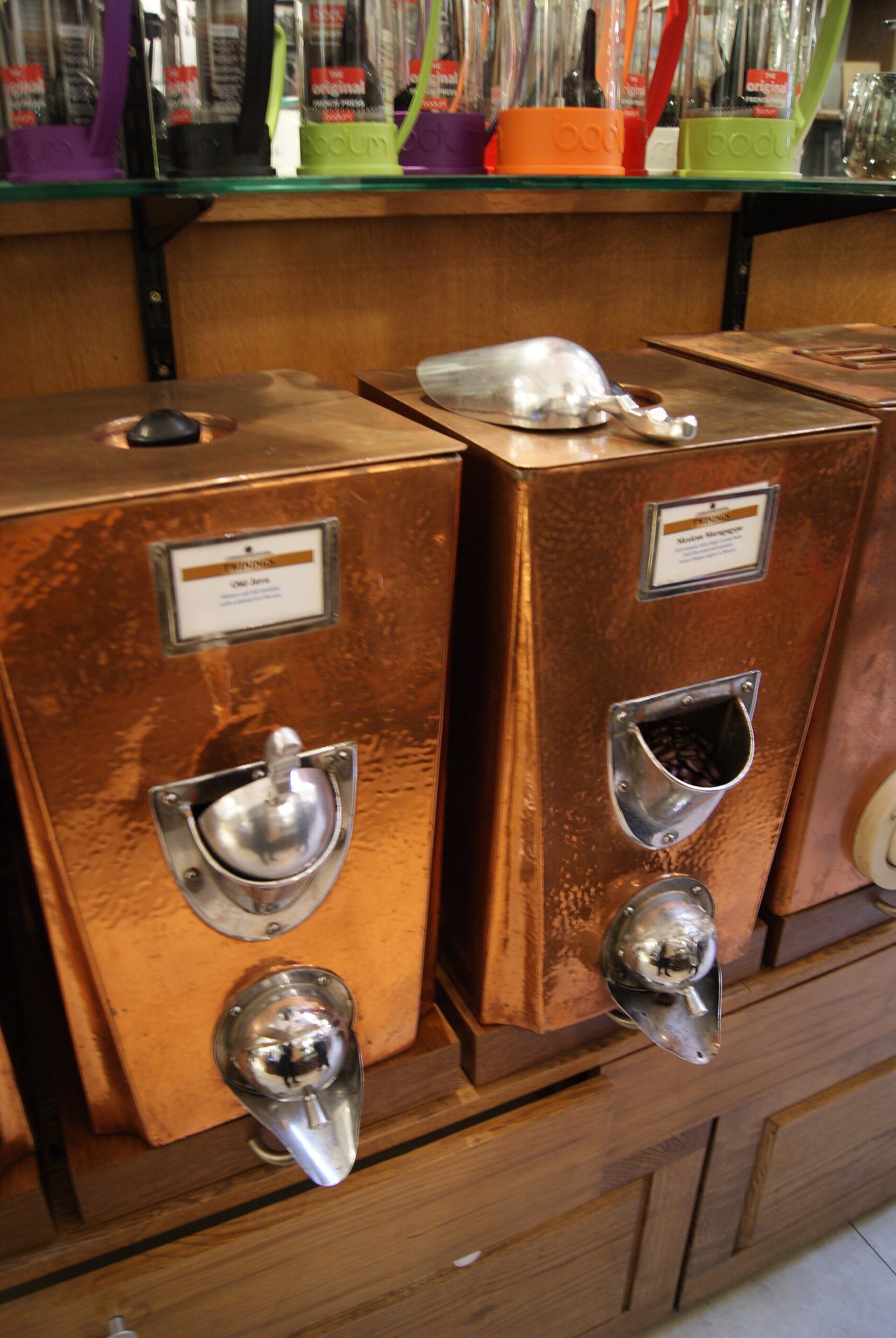 Polished copper tea canisters with brass scoops on wooden shelves inside the Twinings shop.