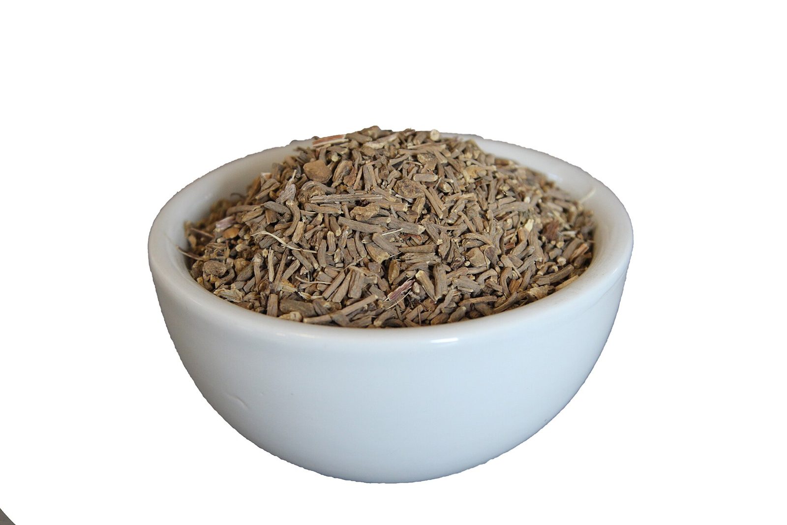 A small white bowl filled with dried, chopped pale brown valerian root pieces.
