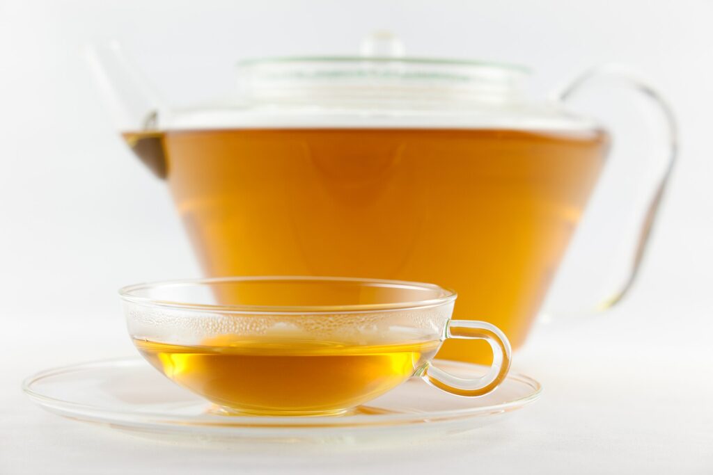 A glass teapot and a small glass cup of clear golden White Peony tea on a white background.