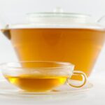 A glass teapot and a small glass cup of clear golden White Peony tea on a white background.