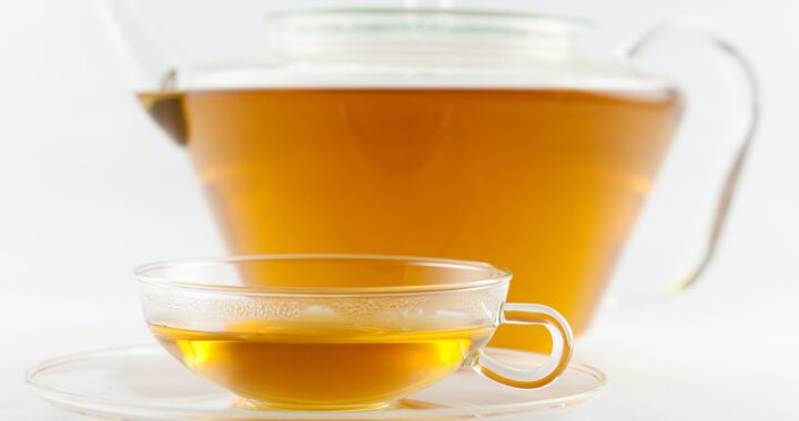 A glass teapot and a small glass cup of clear golden White Peony tea on a white background.